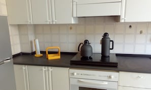 Cozinha com armários brancos, bancada preta e cafeteira.