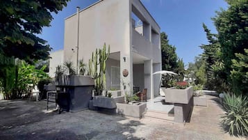 A modern building with a flat roof, surrounded by various plants and trees.
