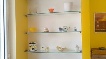 A room with a white radiator, glass shelves with various kitchenware, and a yellow wall.
