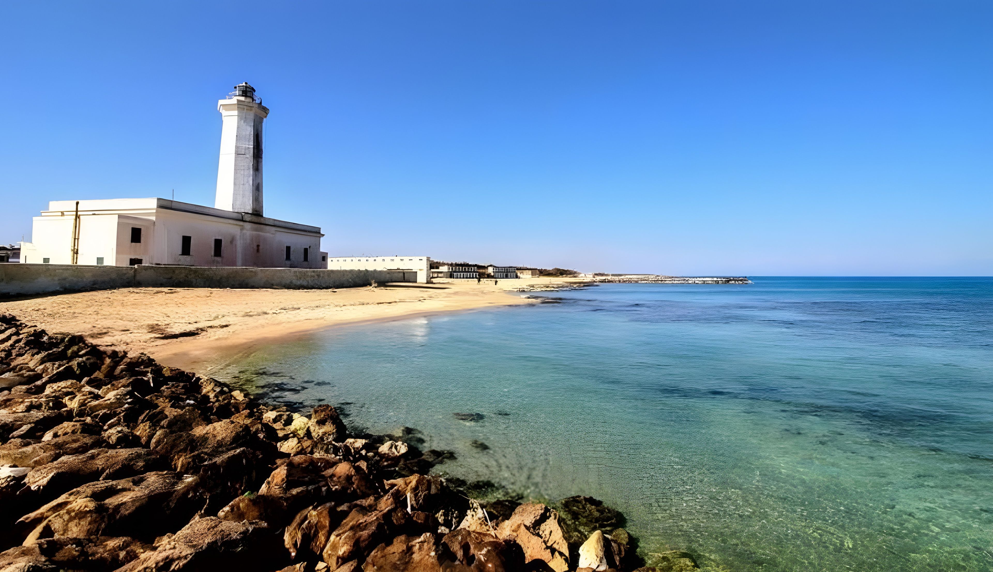 A coastal scene with a lighthouse, clear waters, and a sandy beach.
