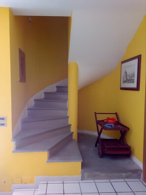 Una escalera conduce a un rellano con una pared amarilla, un cuadro enmarcado y una pequeña mesa con objetos encima.