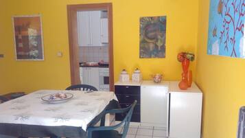 Cozinha compacta com armários brancos, mesa de jantar com cadeiras e uma geladeira pequena.