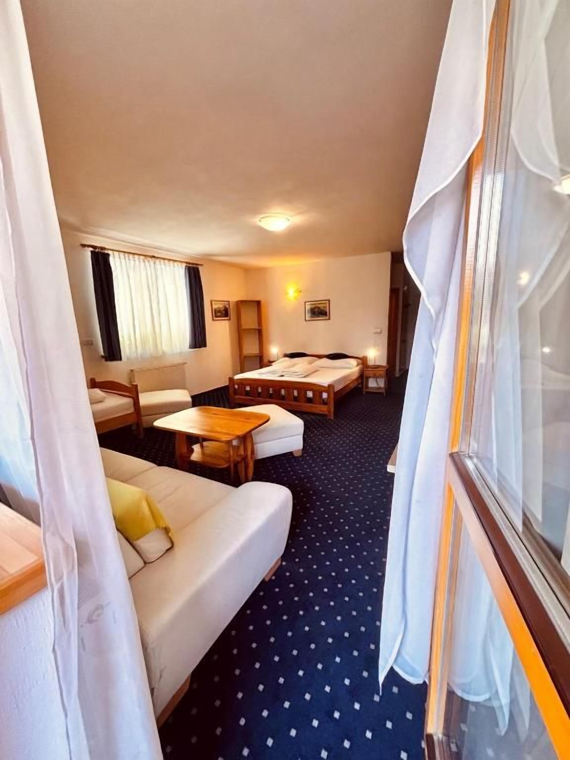 A compact room with a sofa, a small table, a bed, and a window with curtains.