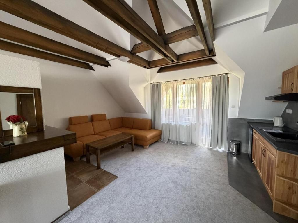 A loft-style living space with a sloped ceiling, a sofa, a coffee table, a kitchen area with wooden cabinets, and a window with curtains.