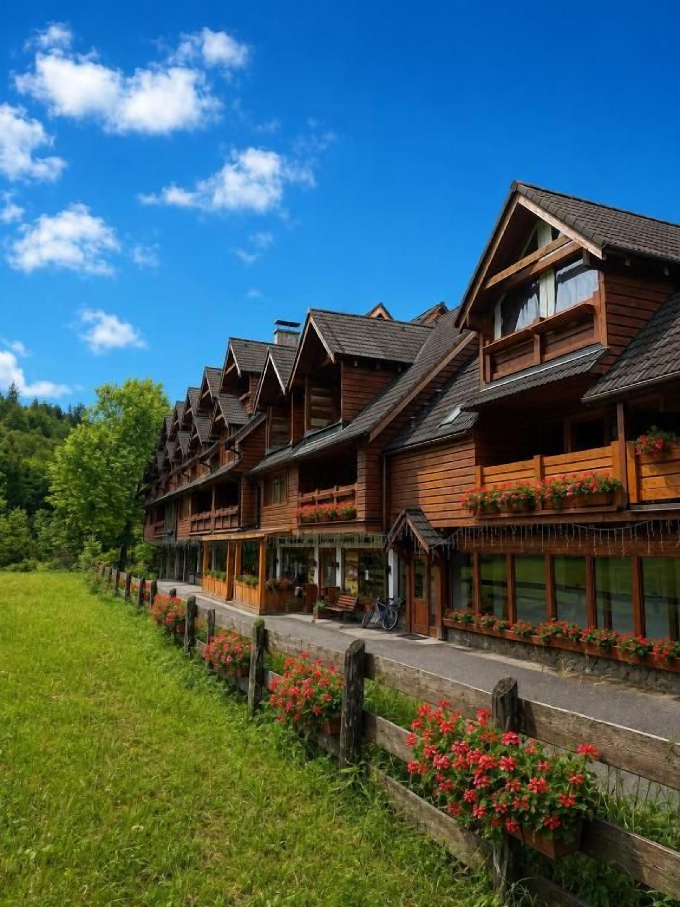 A row of wooden buildings with balconies, a paved walkway, and a grassy area with flowers.