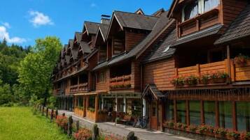 A row of wooden buildings with balconies, a paved walkway, and a grassy area with flowers.
