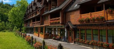 A row of wooden buildings with balconies, a paved walkway, and a grassy area with flowers.