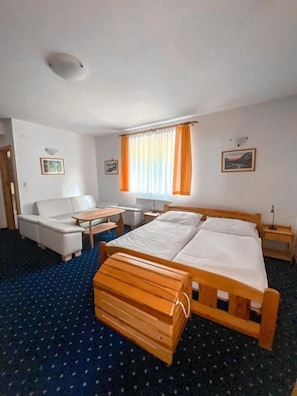 A hotel room with a bed, a sofa, a small table, and a window with curtains.