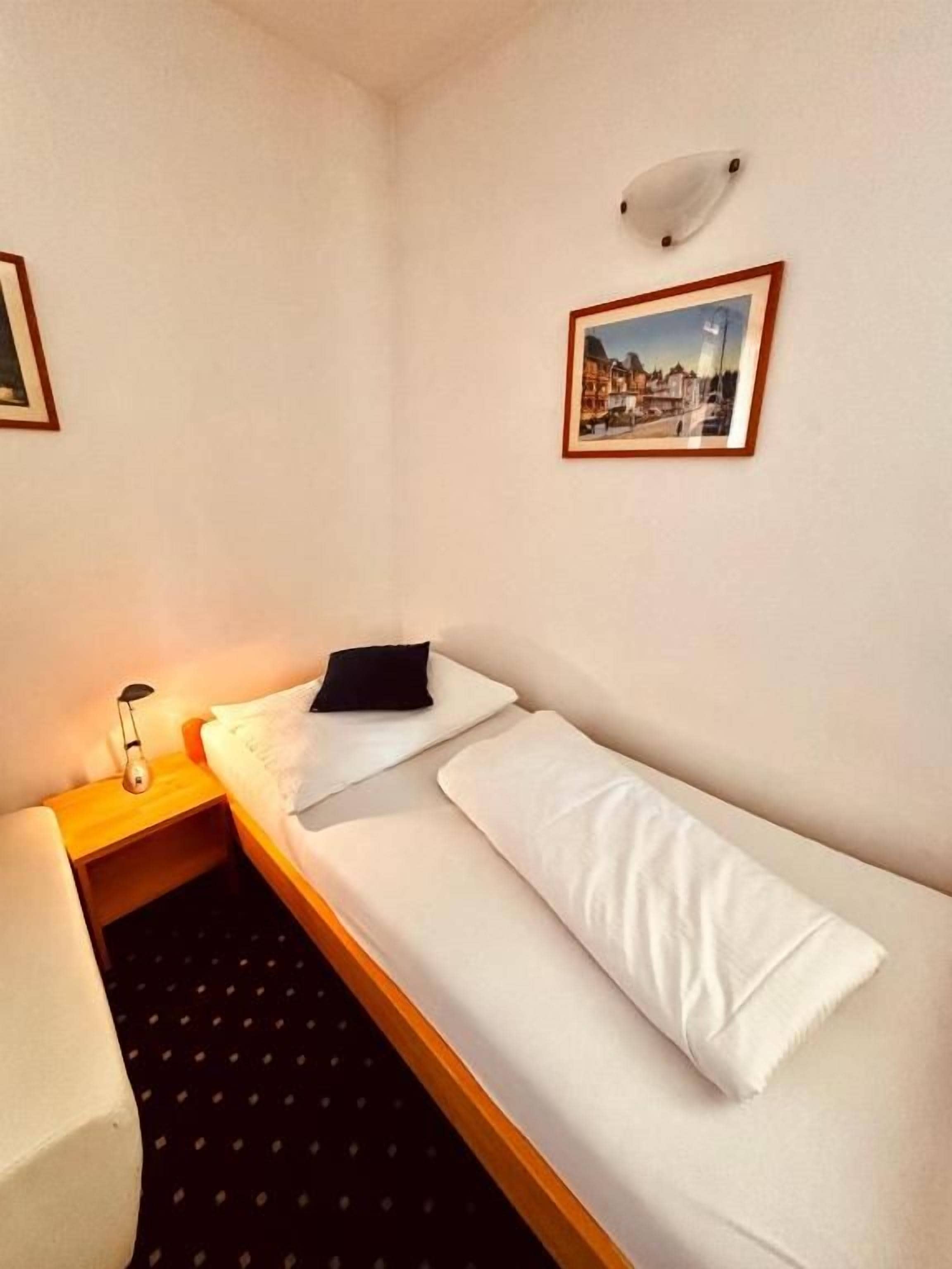A single bed with white linens, a bedside table with a lamp, and a framed picture on the wall.
