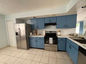 A kitchen with blue cabinets, a stainless steel refrigerator, and a black oven. - Summer Tree Suites (Jacksonville)