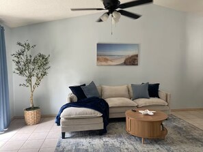 A living room with a sofa, ottoman, coffee table, and a ceiling fan. - Summer Tree Suites (Jacksonville)