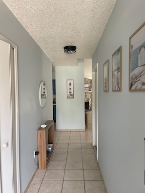A hallway with a tiled floor, a wooden bench, and framed pictures on the walls. - Summer Tree Suites (Jacksonville)