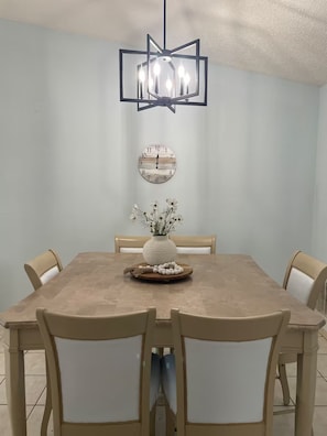 A dining room with a rectangular table, six chairs, a chandelier, a wall clock, and a vase with flowers. - Summer Tree Suites (Jacksonville)