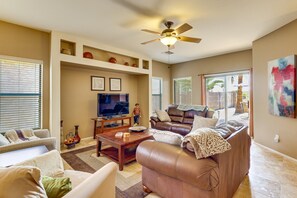 A living room with a television, leather sofa, and a ceiling fan. - Enjoy breathtaking sunrises and sunsets on Johnson Ranch golf course and unforgettable stargazing from the peaceful backyard. (San Tan Valley)