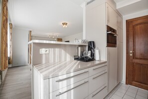 A modern kitchen with white cabinetry, a built-in oven, and a coffee machine. - Hill Apartment With Park Views (Blankenberge)