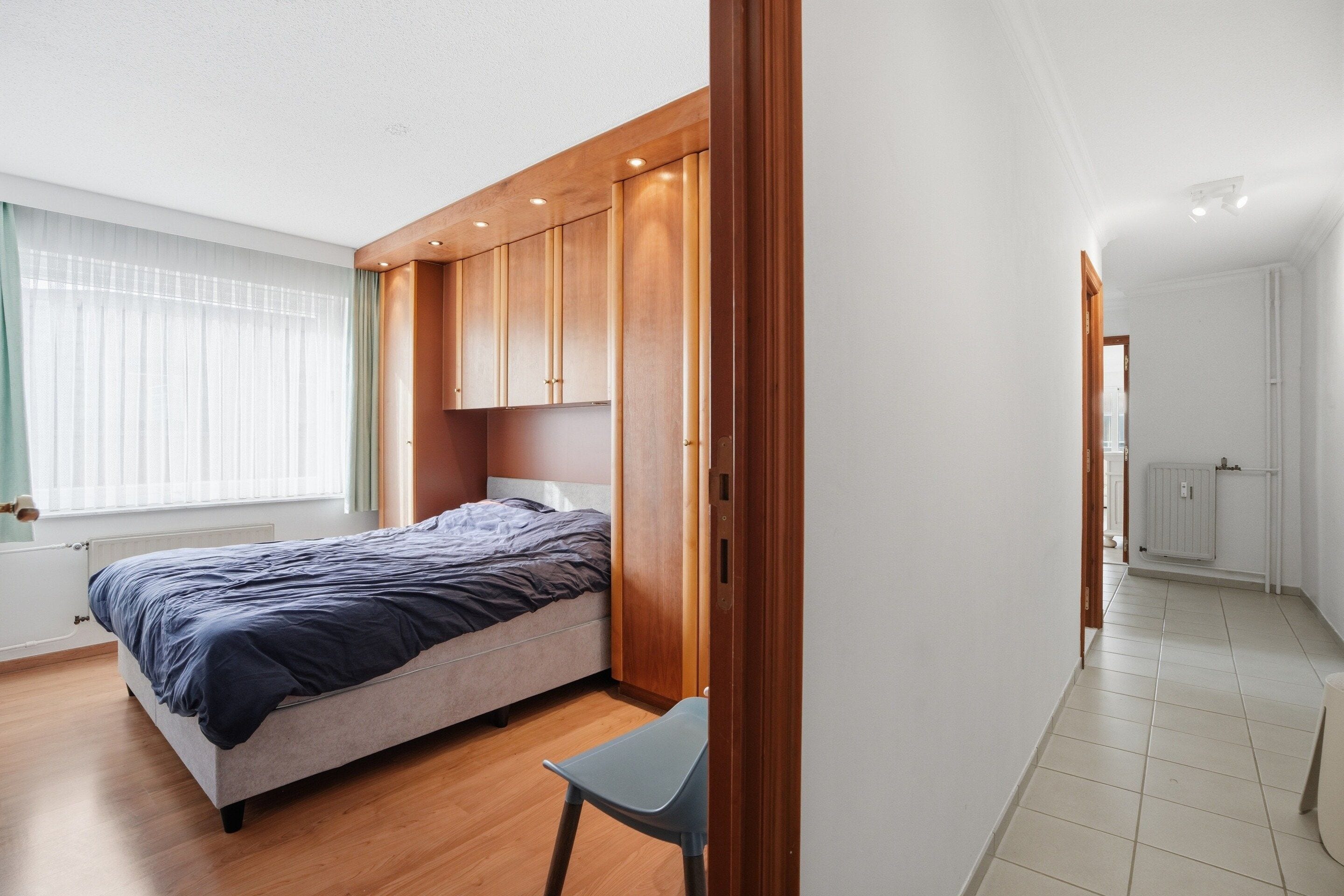A bedroom with a bed, wooden wardrobe, and a chair.