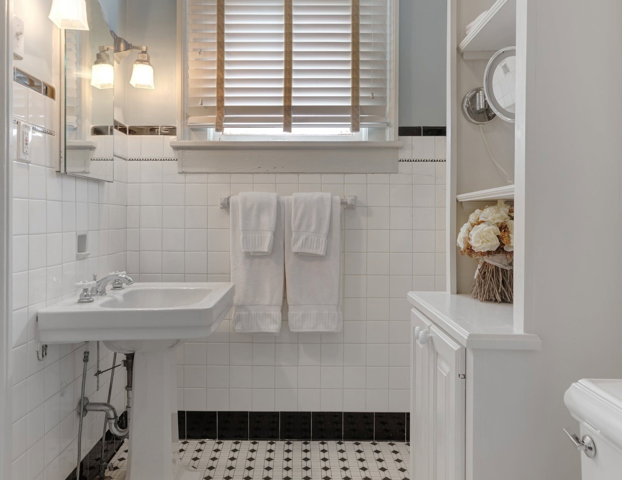 A bathroom with a white sink, a mirror, and a window with blinds.
