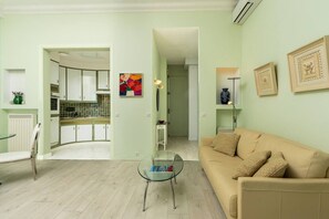 Una sala de estar con un sofá color beige, una mesa de centro de vidrio y una cocina visible a través de un umbral abierto.