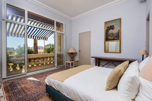 A hotel room with a bed, a desk, a chair, a lamp, a painting, and a view through a glass door. - Belle Époque Flat with Garden & Sea View - Cannes (Cannes)