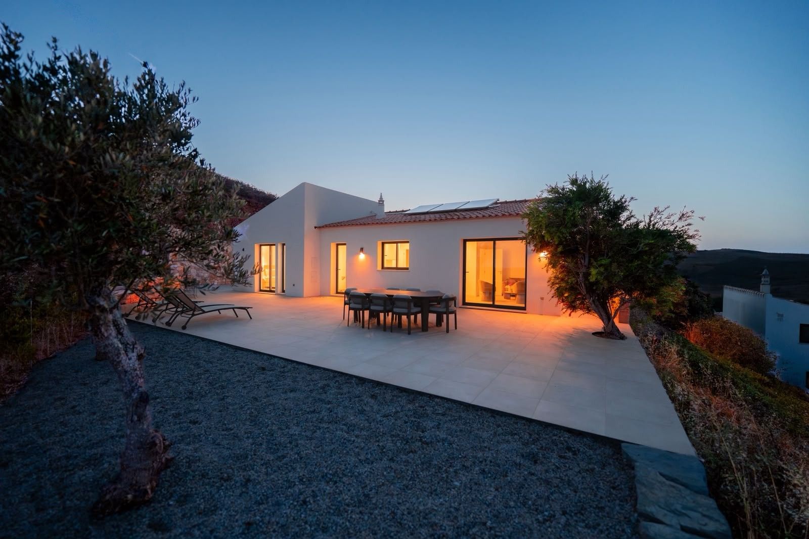 A modern house with a patio, a dining area, and a view of the surrounding landscape.