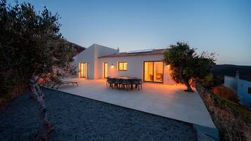 A modern house with a patio, a dining area, and a view of the surrounding landscape.