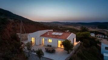 Ein modernes Haus mit flachem Dach und großen Fenstern, eingebettet in eine hügelige Landschaft.