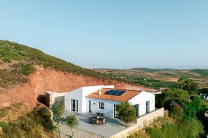 A modern house with a solar panel roof, a patio with a table and chairs, and a view of the surrounding landscape.