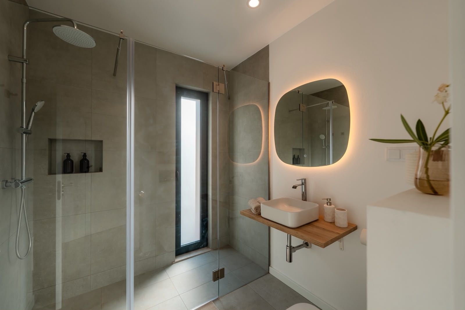 Ein modernes Badezimmer mit einer gläsernen Dusche, einem großen Spiegel mit beleuchtetem Rahmen und einem Holzbadezimmermöbel mit Waschbecken.