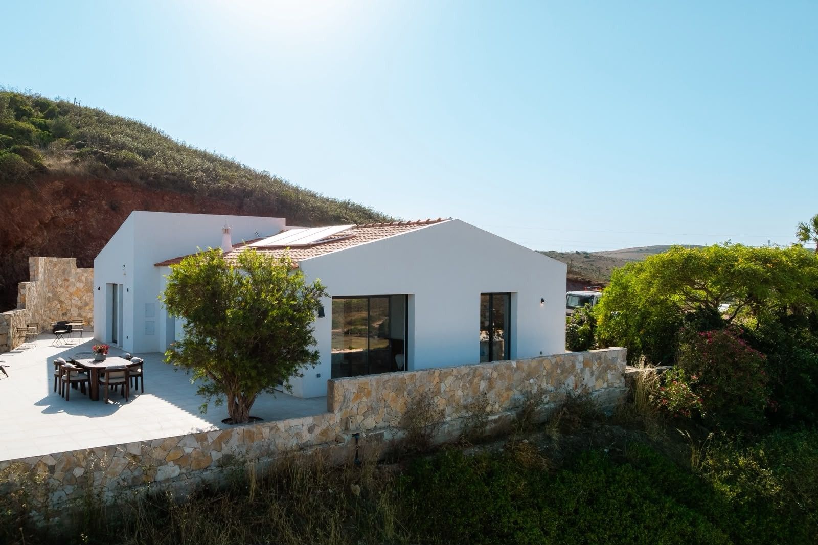 Un edificio moderno de color blanco con techo plano, pared de piedra y un patio con mobiliario exterior.