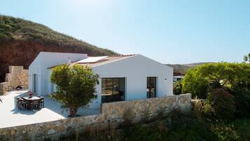 Un edificio moderno de color blanco con techo plano, pared de piedra y un patio con mobiliario exterior.