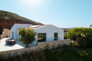 Edifici modern blanc amb teulada plana, mur de pedra i un patí amb mobles de jardí.