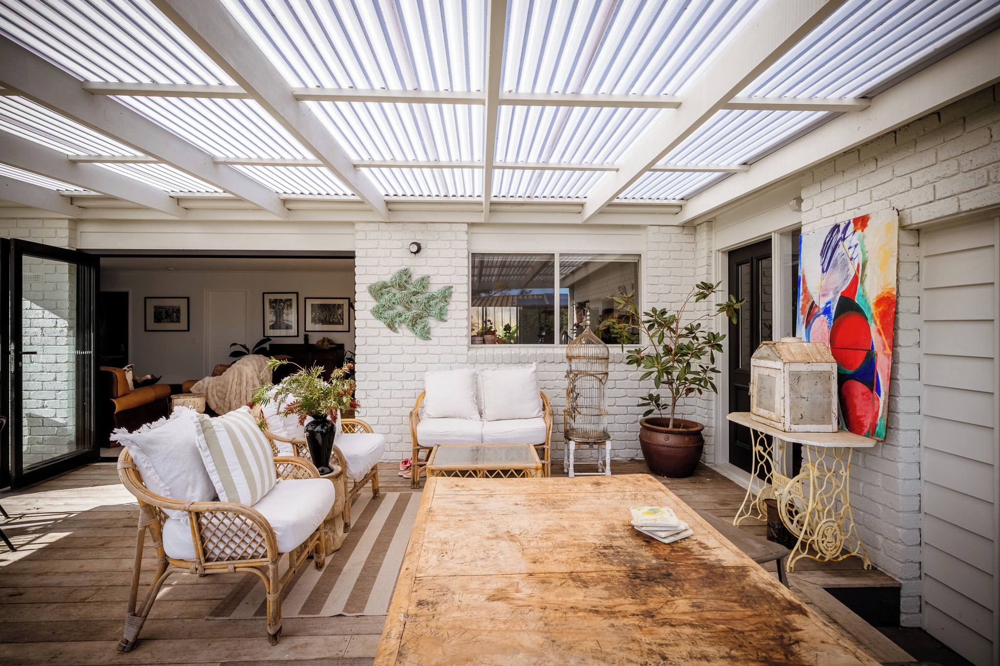 Une vaste terrasse dotée d’une table en bois, de meubles en osier et d’une plante en pot.