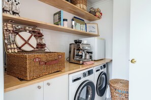 Une cuisine équipée d’un lave-linge, d’une machine à café et de paniers en osier.