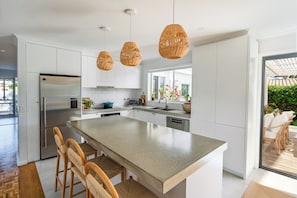 Une cuisine moderne dotée d’un grand îlot central, d’appareils électroménagers en acier inoxydable et de luminaires suspendus en osier.