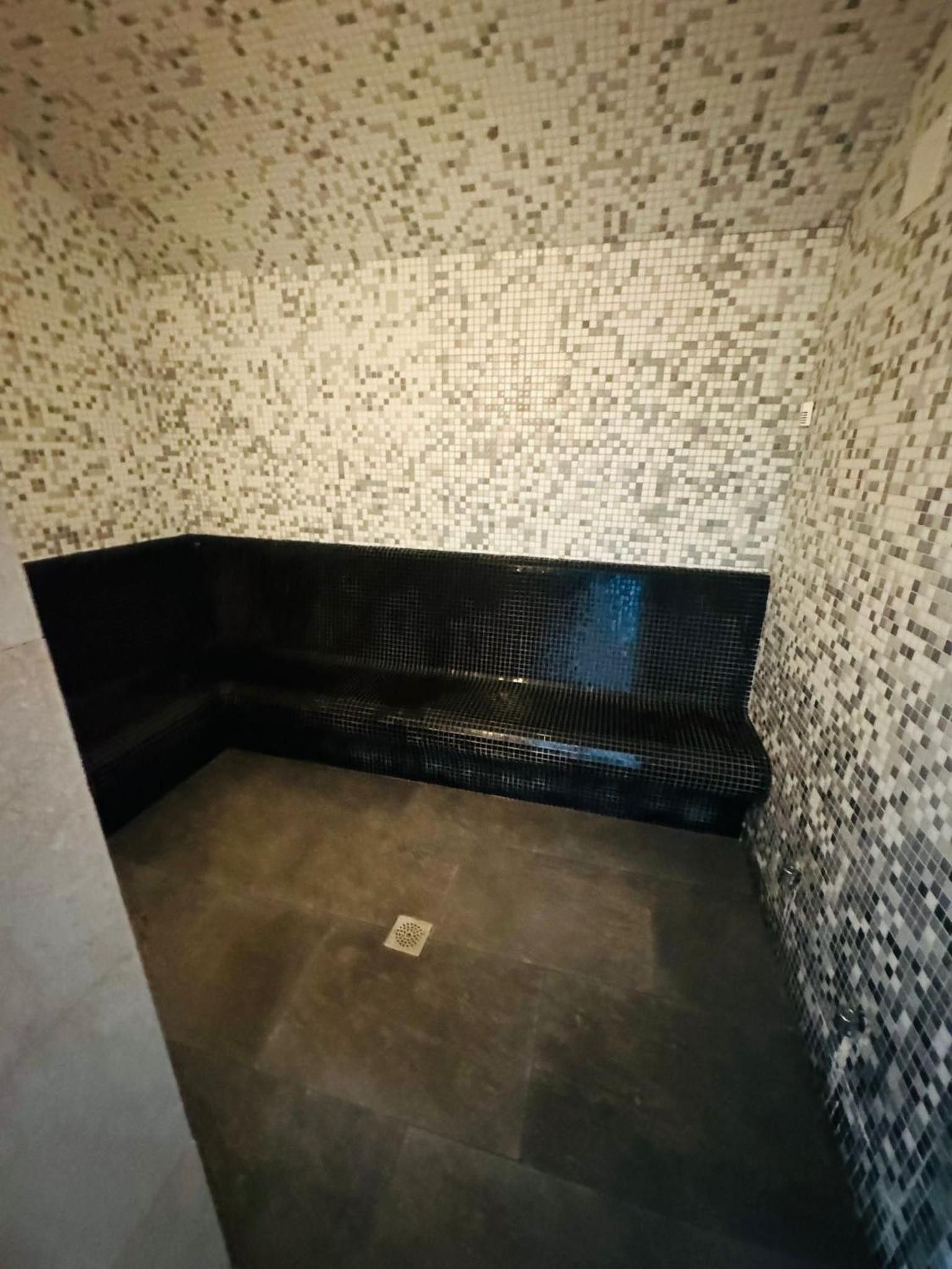 Een klein, donker bad met betegelde wand en vloer.