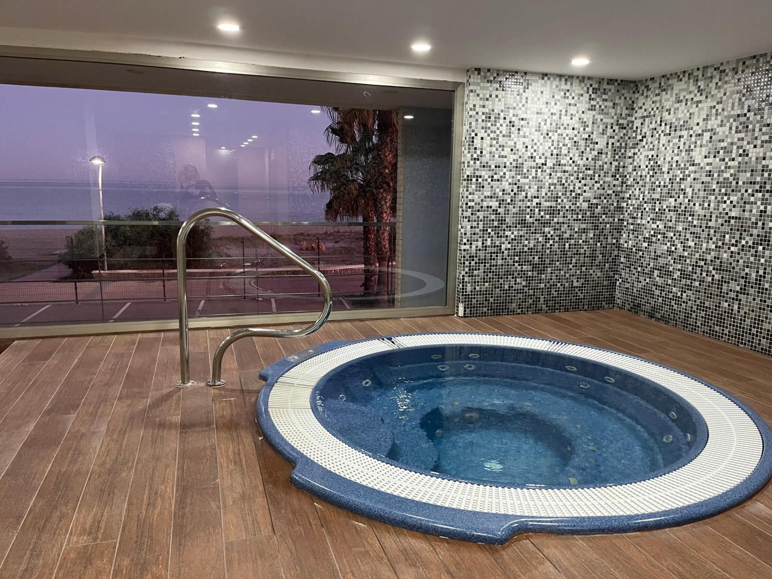 Ein Whirlpool in einem Raum mit großem Fenster, einer Metallreling und einer gefliesten Wand.