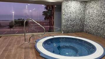 Ein Whirlpool in einem Raum mit großem Fenster, einer Metallreling und einer gefliesten Wand.