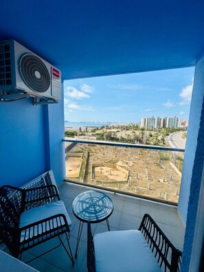 A balcony with a view of a cityscape, a table, and a chair.