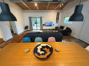 A modern living room with a wooden dining table, a large sofa, and a television. - PRD 2420 Rio Vista: Escape to the beautiful Guadalupe River (New Braunfels)