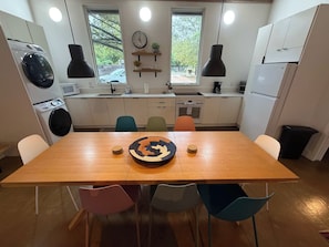 A modern kitchen with a central island, white cabinets, and a dining area with colorful chairs. - PRD 2420 Rio Vista: Escape to the beautiful Guadalupe River (New Braunfels)