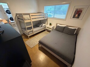 A compact bedroom with bunk beds, a single bed, a small bedside table with a plant, and a window with blinds. - PRD 2420 Rio Vista: Escape to the beautiful Guadalupe River (New Braunfels)