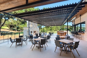 Eine Außenpatio-Terrasse mit Tischen, Stühlen, einer Pergola und Blick auf die umliegende Landschaft.
