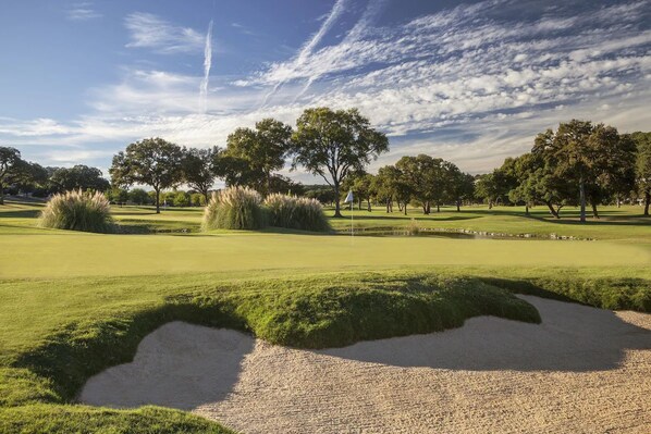 Ein Golfplatz mit Sandbunkern, Bäumen und blauem Himmel.