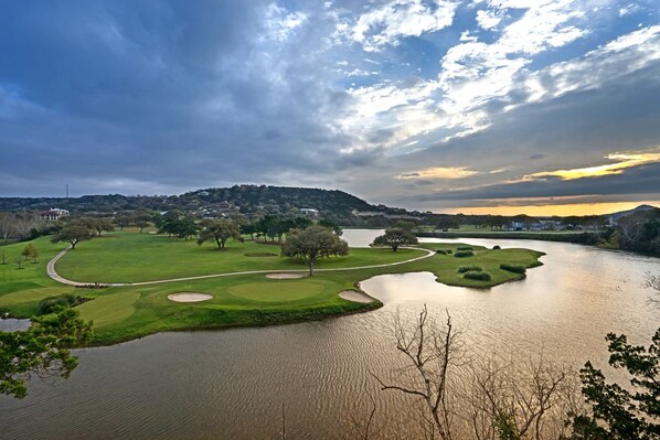 Ein Golfplatz mit See, Bäumen und einer entfernten Hügelkette mit Gebäuden.