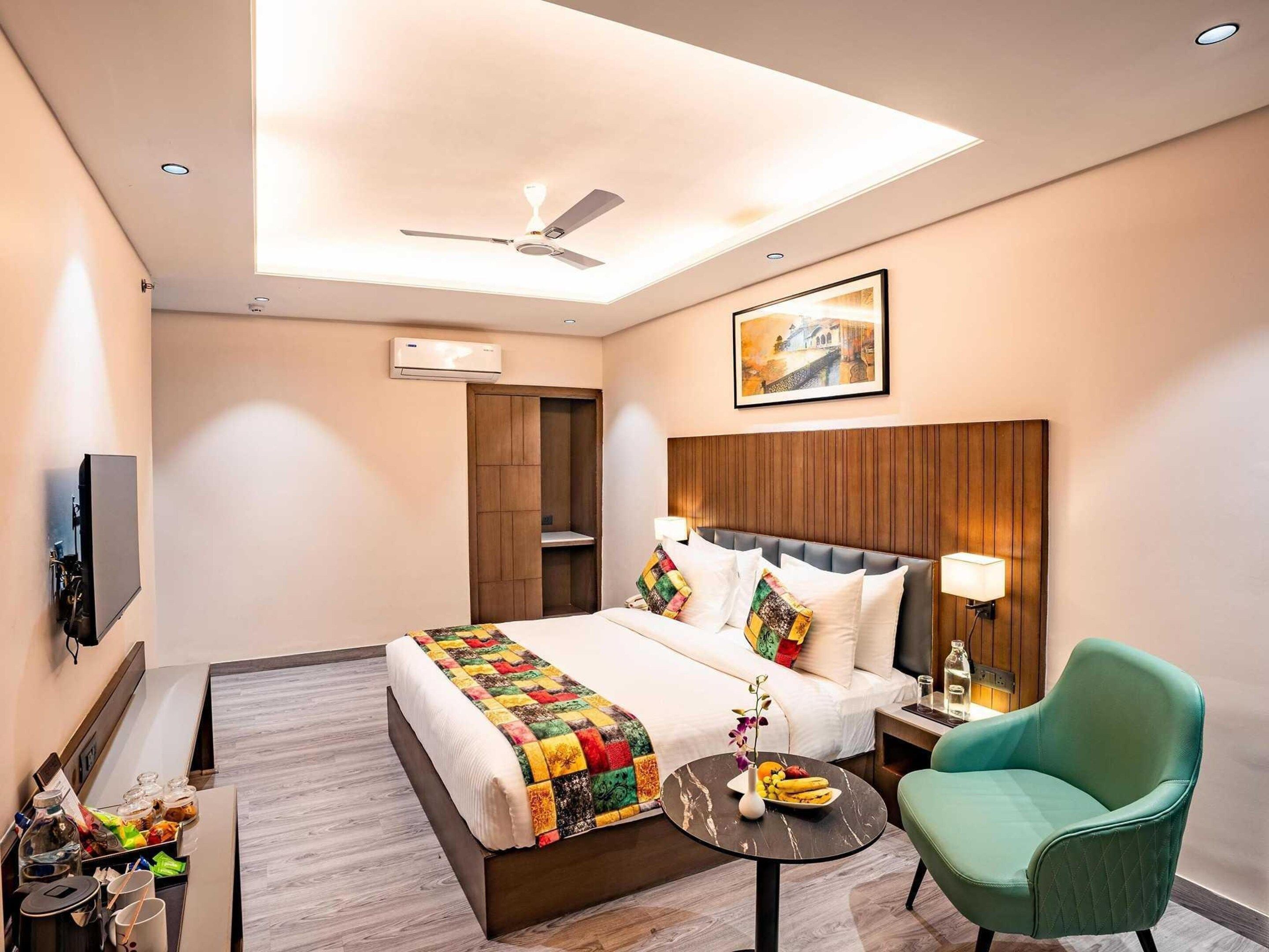 Een hotelkamer met een bed, een bureau, een stoel, een plafondventilator, een airconditioner en een schilderij aan de muur.