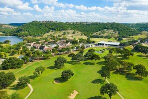 Eine Vogelperspektive eines Golfplatzes mit Clubhaus, Wohnhäusern und einem See im Hintergrund.