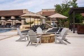 Ein Poolbereich mit Adirondack-Stühlen, einer Feuerstelle und Sonnenschirmen.
