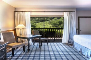 Ein Hotelzimmer mit Schachbrettmuster-Boden, einem Bett, einem Tisch mit Stühlen, einer Lampe und einem Balkon mit Vorhängen.