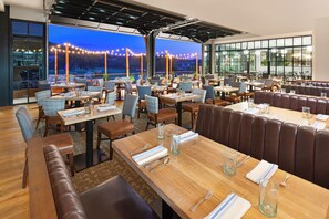 Ein Restaurant mit mehreren Tischen und Sitzecken, großen Fenstern mit Bergblick und Lichterketten.