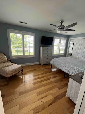 Une chambre à coucher avec un lit, un téléviseur, une chaise et un ventilateur de plafond.